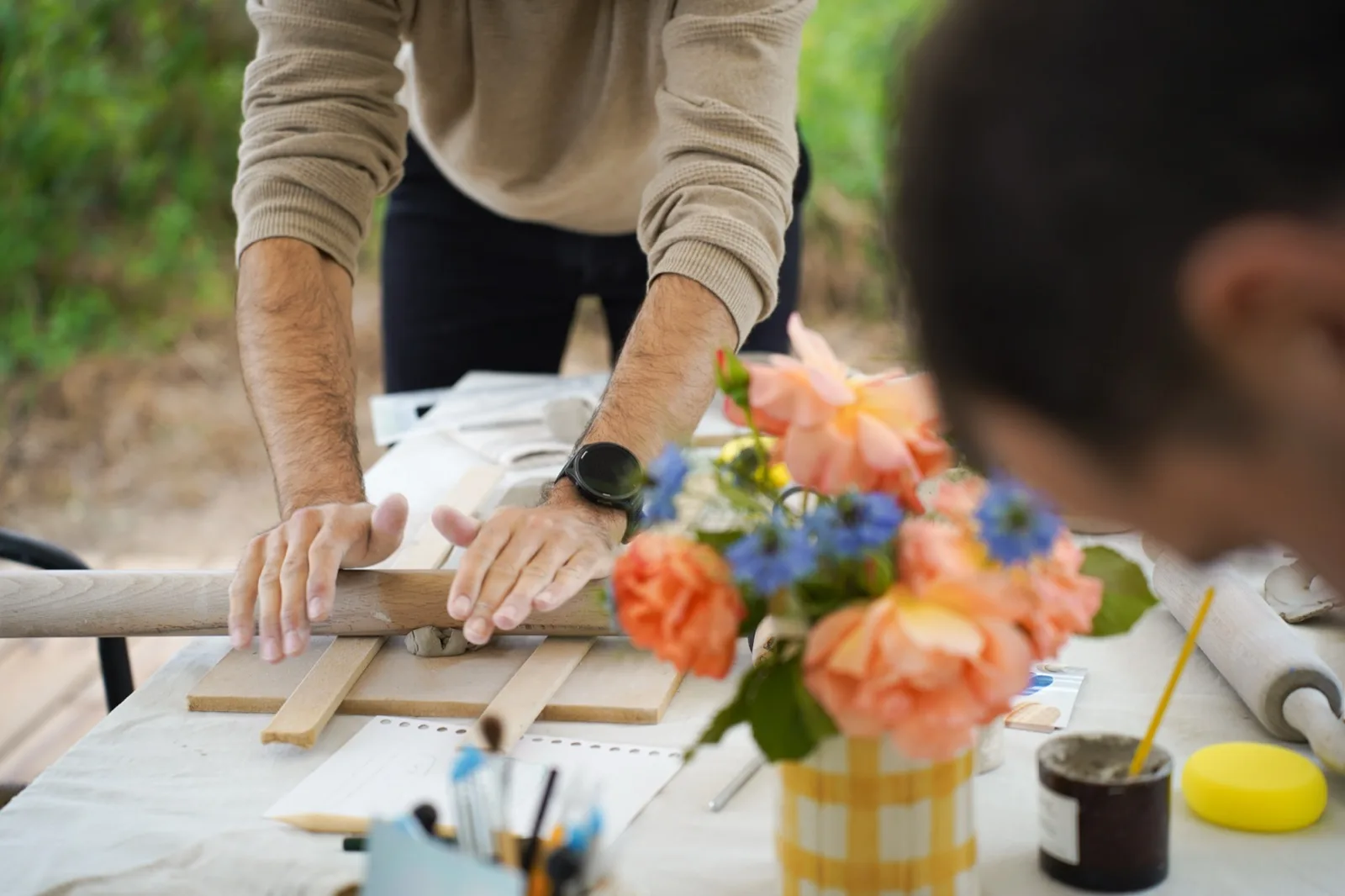 Un participant abaisse une plaque de terre au rouleau, un bouquet posé sur la table