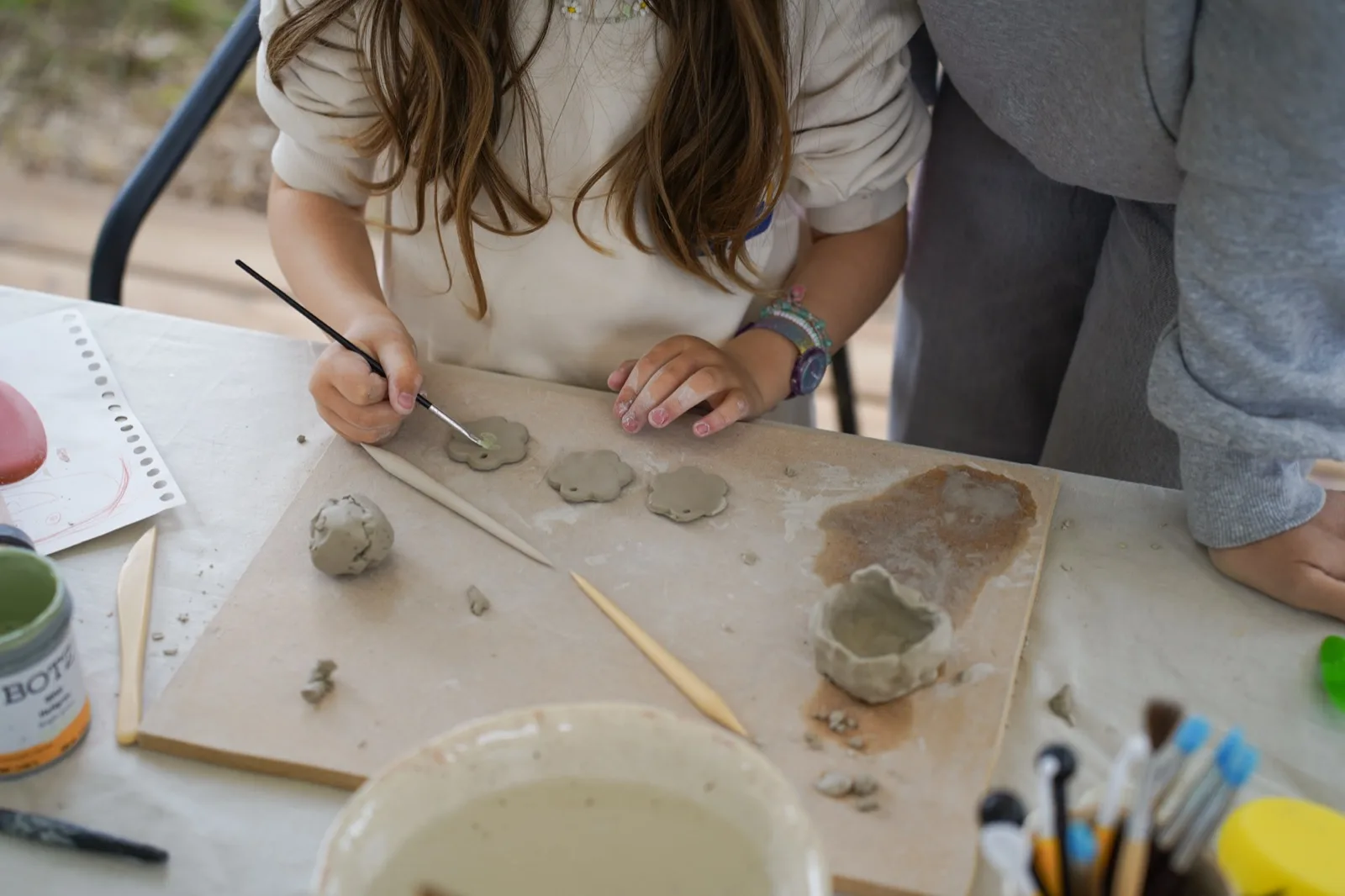 Une enfant découpe des formes dans une plaque de terre à l’atelier en extérieur